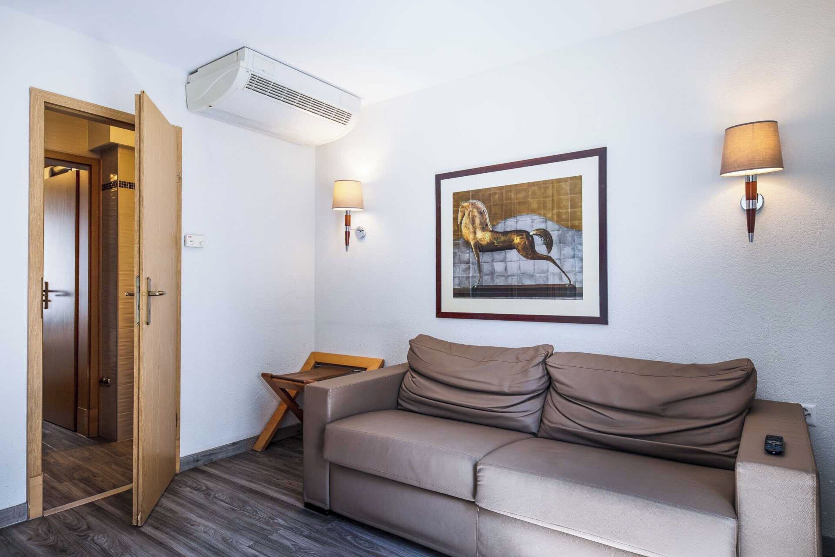 Una habitación con un sofá color beige, una obra de arte enmarcada en la pared, una puerta de madera y una mesita.