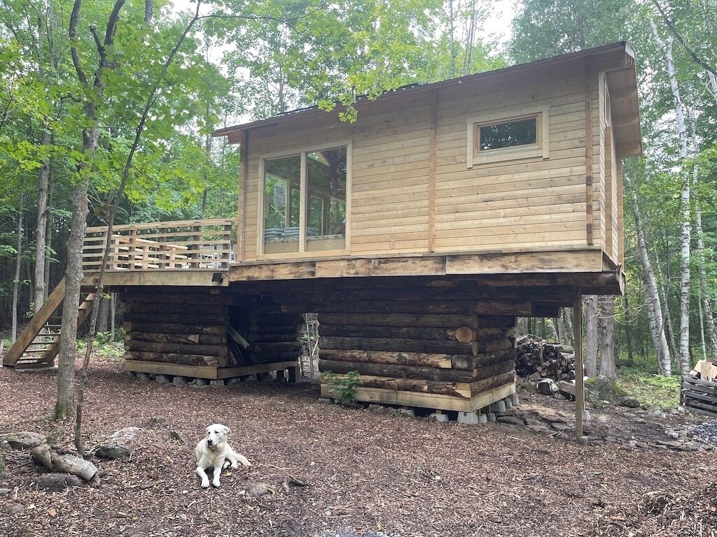 A wooden cabin with a deck, surrounded by trees.