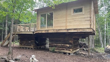 A wooden cabin with a deck, surrounded by trees.