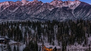 A lodge with a warm-lit interior, surrounded by a dense forest and snow-covered mountains. - Alpine Luxury | Engineer Mtn View | Pool & Hot Tub (Durango)