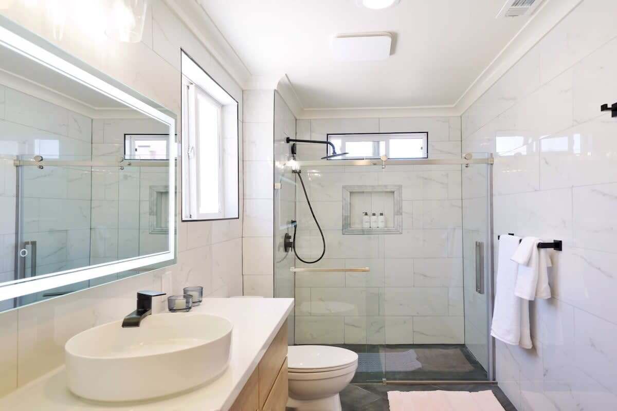 A modern bathroom with a large mirror, a white sink, a toilet, and a glass-enclosed shower area.
