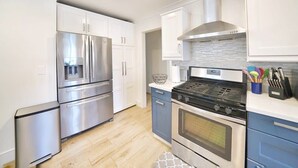 A modern kitchen with stainless steel appliances, white cabinets, and a blue accent wall. - @ Marbella Lane - Vibrant 4BR RWC Ldry + P (Redwood City)