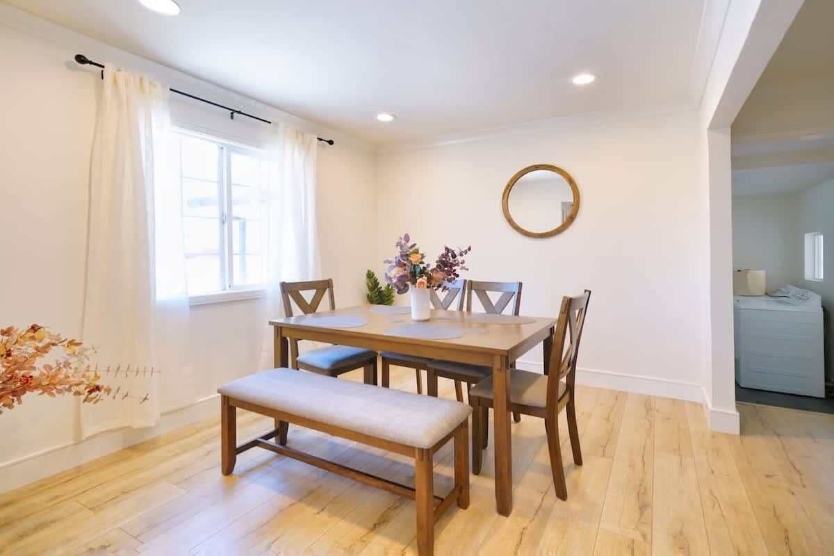 Un comedor con una mesa de madera, cuatro sillas, un banco y un florero.
