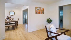 A spacious living area with a wooden floor, a dining table with chairs, a round mirror, and two wall-mounted abstract paintings. - @ Marbella Lane - Vibrant 4BR RWC Ldry + P (Redwood City)
