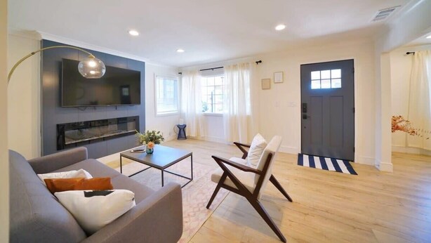 A modern living room with a sofa, coffee table, and a TV mounted on the wall. - @ Marbella Lane - Vibrant 4BR RWC Ldry + P (Redwood City)