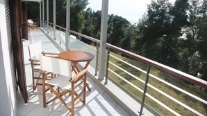 Een balkon met een houten tafel en stoelen, met uitzicht op een grasveld en bomen.