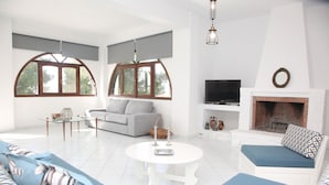 Een moderne woonkamer met een witte bank, een grijze bank, een ronde salontafel en een open haard.
