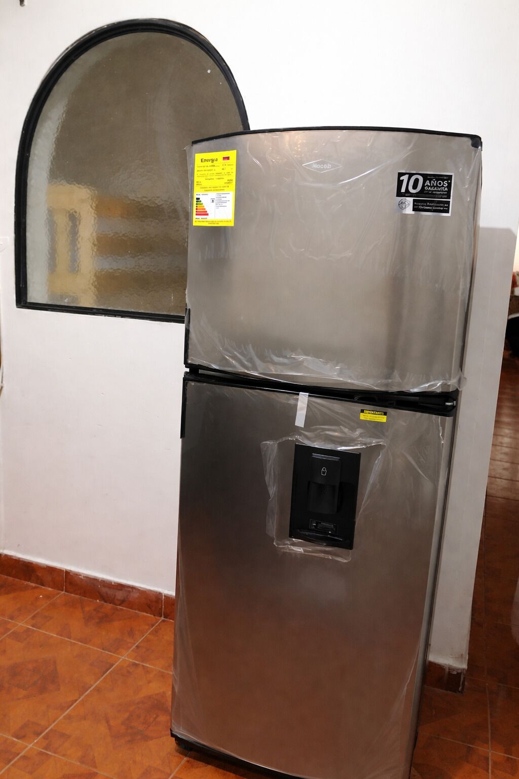 Un refrigerador de acero inoxidable con compartimento congelador y dispensador de agua, y una etiqueta de garantía de 10 años.