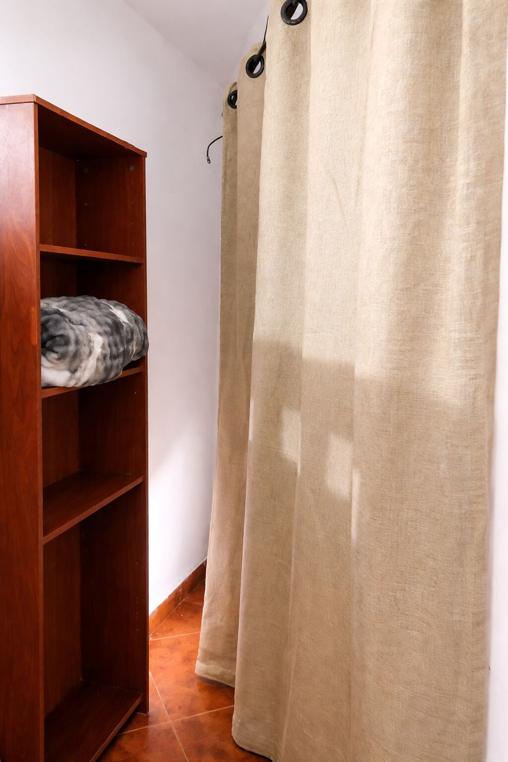 A wooden shelf with a folded blanket and a beige curtain with a ring.