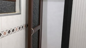 Un baño con azulejos blancos, una zona de ducha con puerta de cristal y un borde de azulejos estampados.