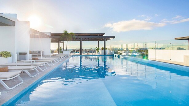 A rooftop infinity pool with lounge chairs and a pergola, offering a clear view of the city skyline. - Stylish 2Bd Condo, Rooftop Oasis in Playa del Carmen (Playa Del Carmen)
