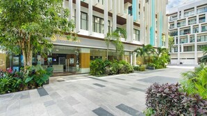A modern hotel with a glass facade, outdoor seating area, and lush greenery. - Stylish 2Bd Condo, Rooftop Oasis in Playa del Carmen (Playa Del Carmen)