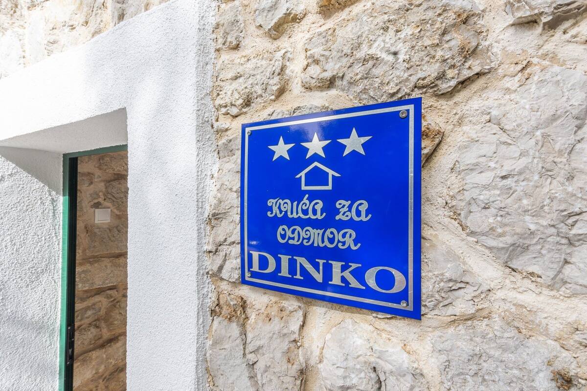 A blue sign with white text and stars, mounted on a stone wall.