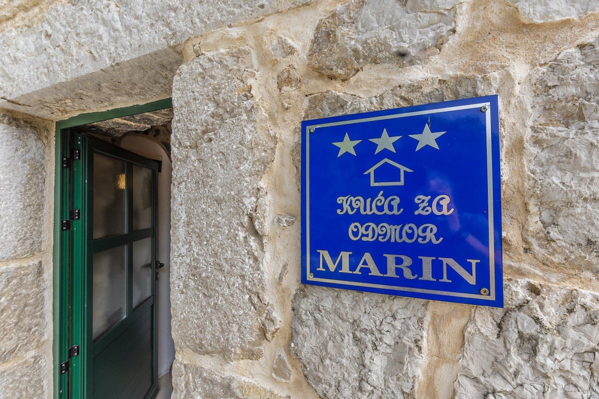 A stone wall with a blue sign that reads "Kraljevo od Morin" and a green-framed door.
