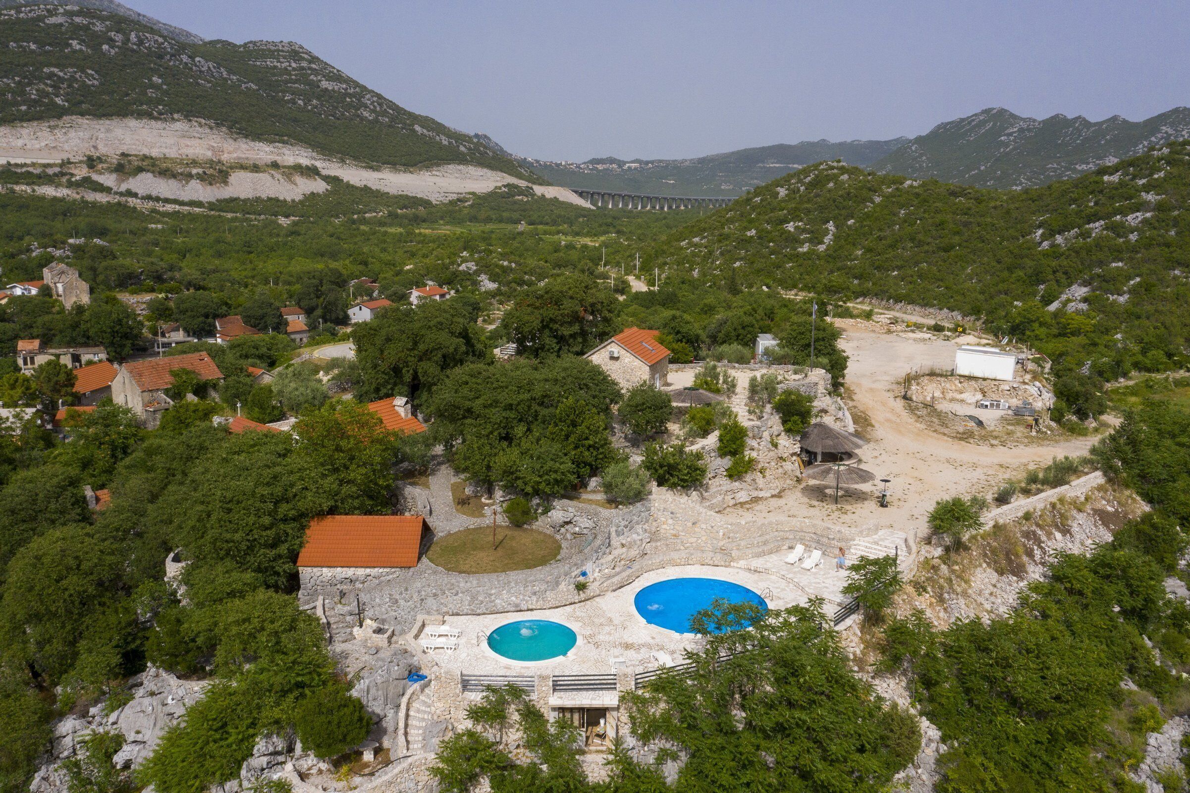 A mountainous area with a swimming pool complex, including two pools and a small building with a red roof.
