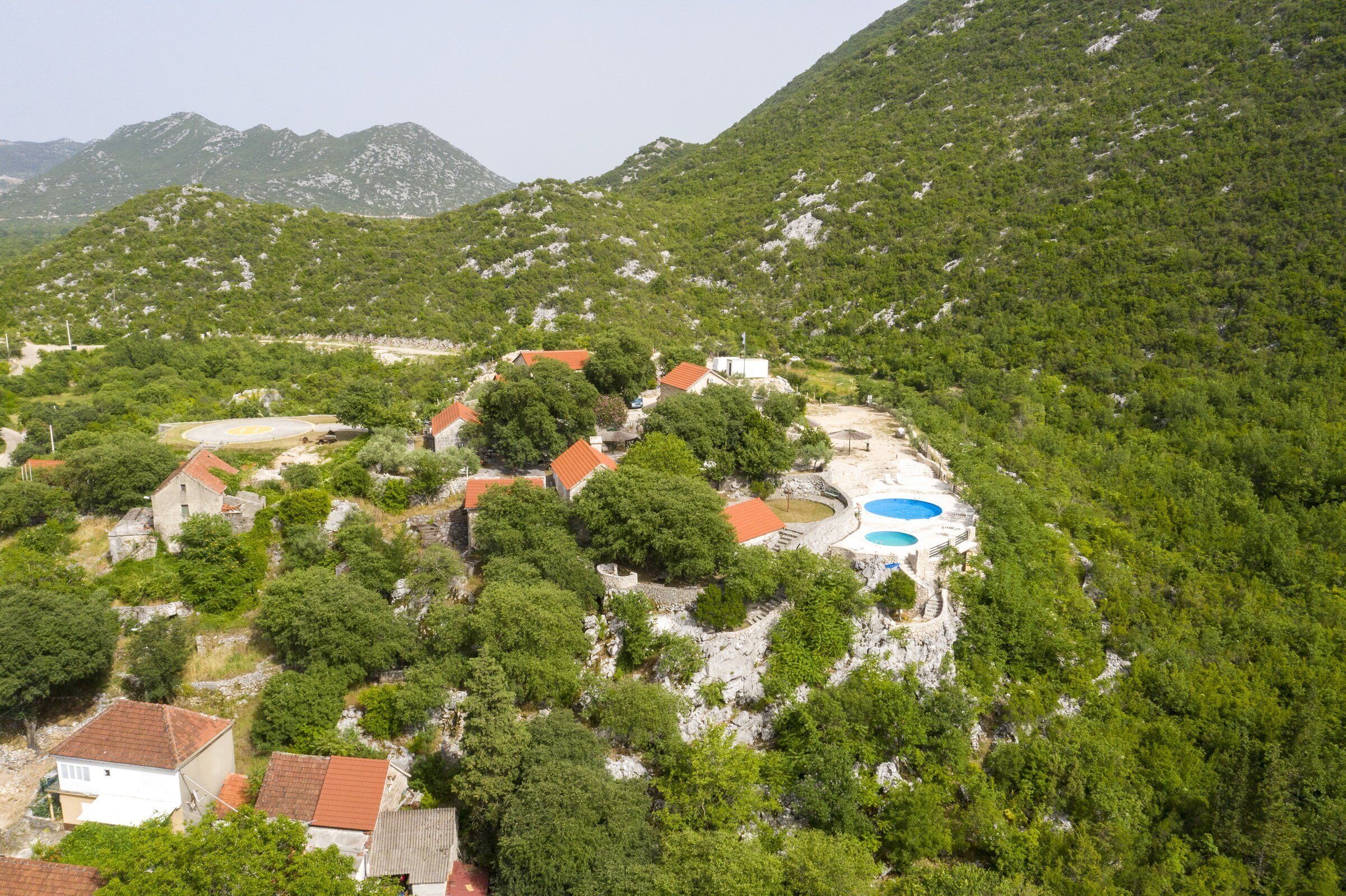 A mountainous area with a cluster of buildings surrounded by dense greenery and rocky terrain.