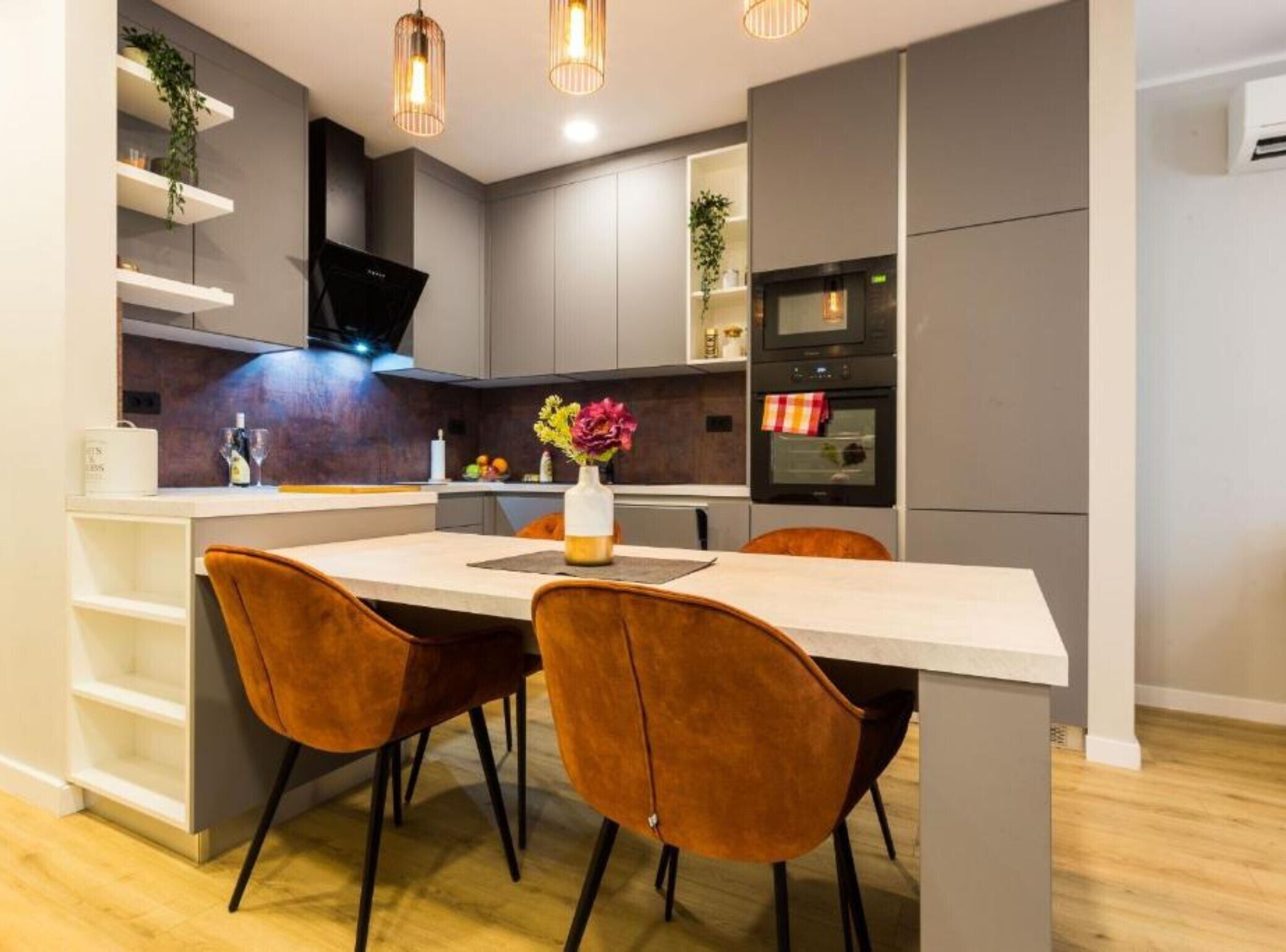 A modern kitchen with a white countertop, two brown chairs, and a vase with flowers.