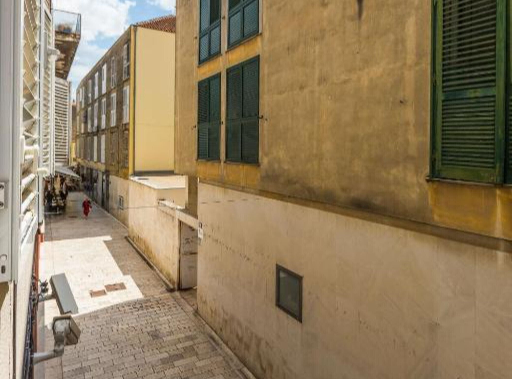 Une ruelle étroite bordée de bâtiments des deux côtés, avec un chemin pavé et un petit banc.