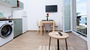 Une cuisine compacte équipée d’un lave-linge, un coin repas avec une table et des chaises, et un téléviseur fixé au mur.