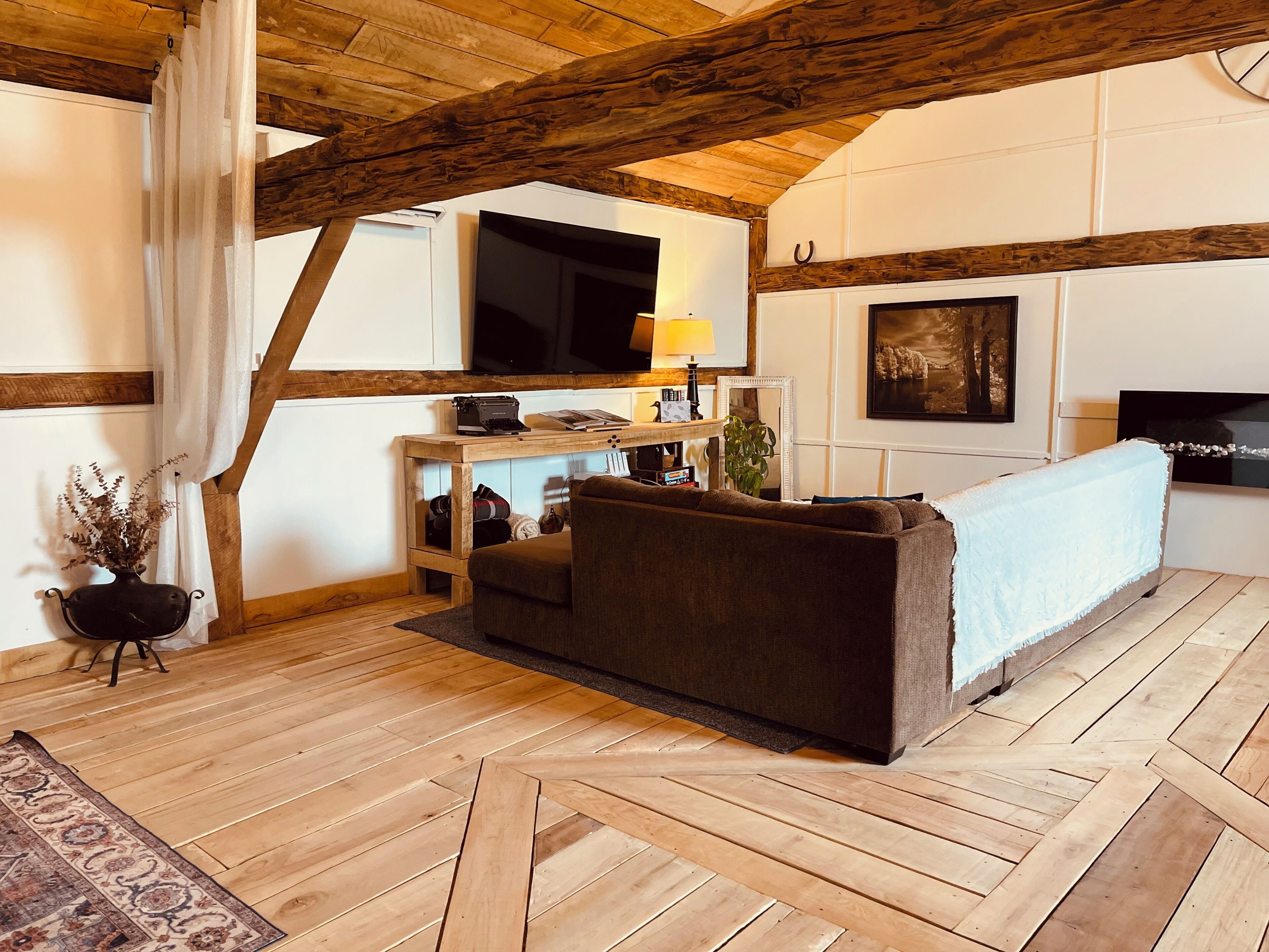 A cozy room with a wooden ceiling, a sofa, a television, and a small table with a lamp.