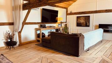 A cozy room with a wooden ceiling, a sofa, a television, and a small table with a lamp.