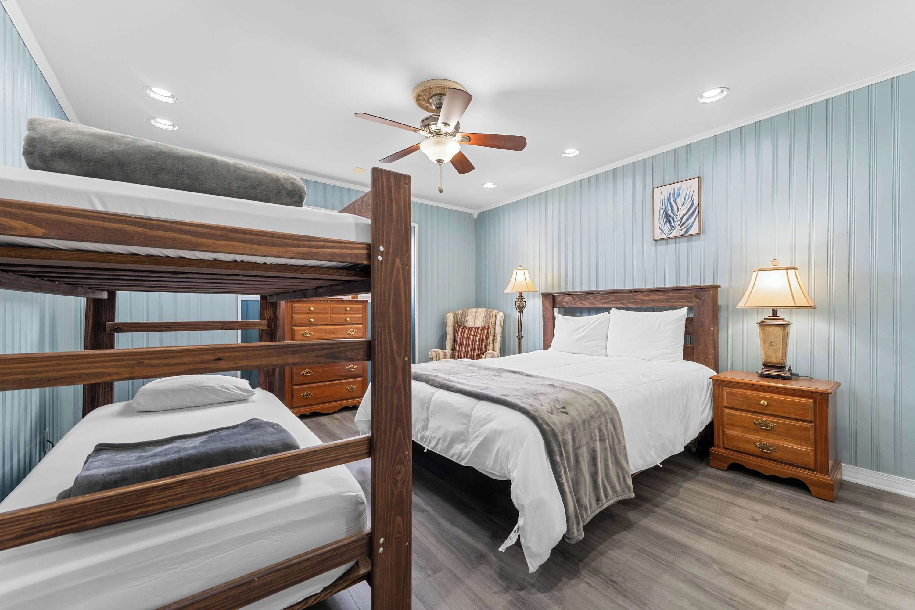 A bunk bed room with a ceiling fan, bedside lamps, a wooden nightstand, and a framed picture on the wall.