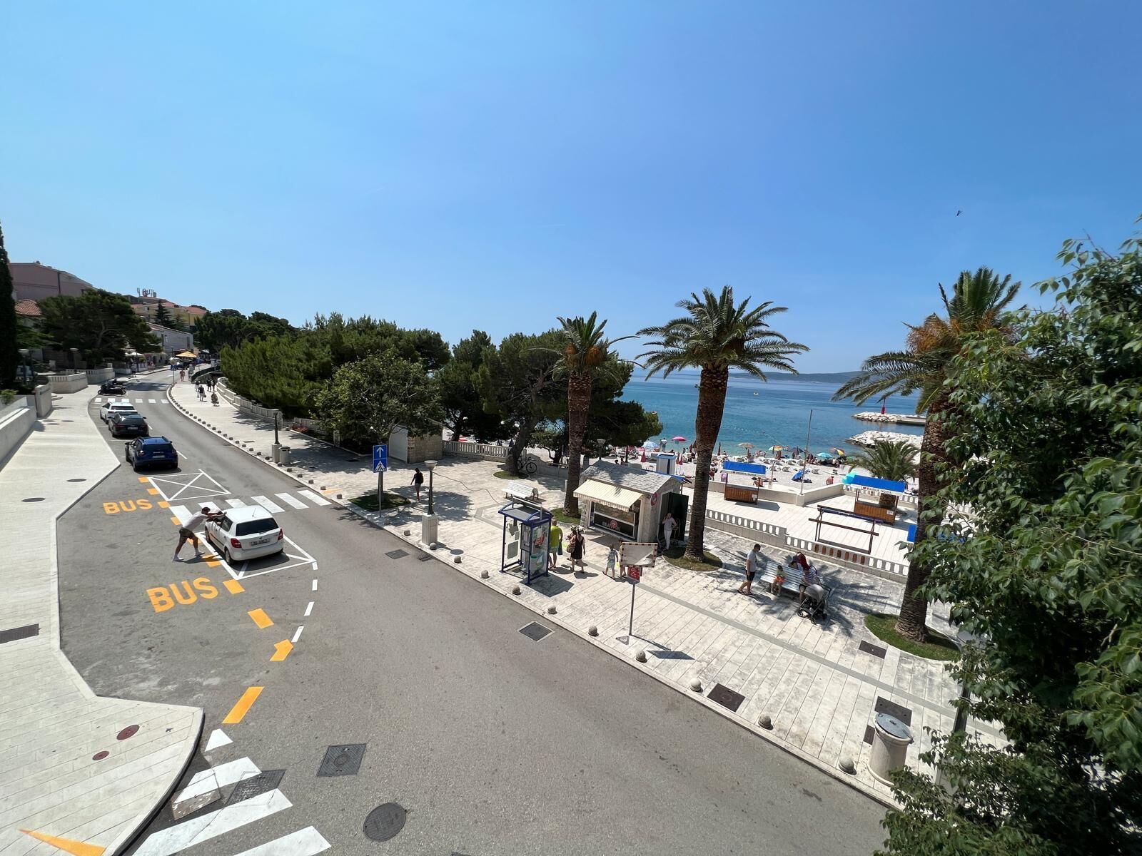 Eine Küstenstraße mit Busspur, Palmen und einem Strand im Hintergrund.
