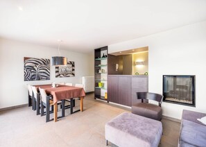 A modern living room with a dining area, a fireplace, and a kitchen visible through an open door. - Apartment in Oostduinkerke With Sea View (Koksijde)