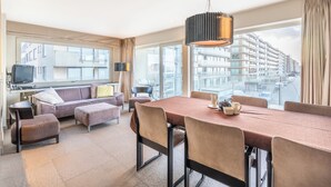 Een moderne hotelkamer met een grote eettafel, comfortabele zitplaatsen, een televisie en uitzicht over de stad.