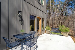 Un edificio moderno con un patio que cuenta con una mesa y sillas de metal, un banco y plantas en macetas.