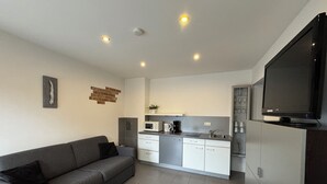 Una cucina moderna con un divano grigio, mobili bianchi e un televisore a schermo piatto.
