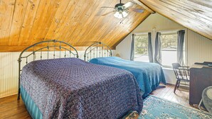 Ein Schlafzimmer mit zwei Betten, einem Deckenventilator, einem Schreibtisch und einem Fenster mit Vorhängen.