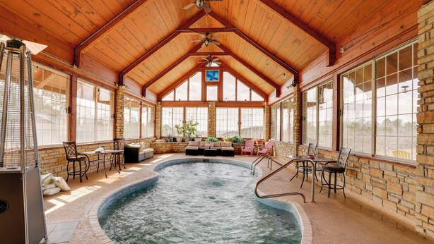 A hot tub in a covered area with wooden beams, stone walls, and large windows. - 366 Shared Acres, Lake Access: Ozark Getaway! (Shirley)