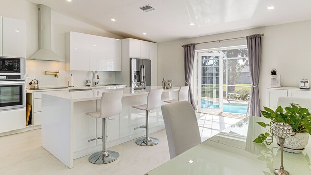 A modern kitchen with white cabinets, a central island with bar stools, a built-in oven, and a refrigerator. - 3 Mi to Beach: Pet-Friendly Home in Port Charlotte (Port Charlotte)