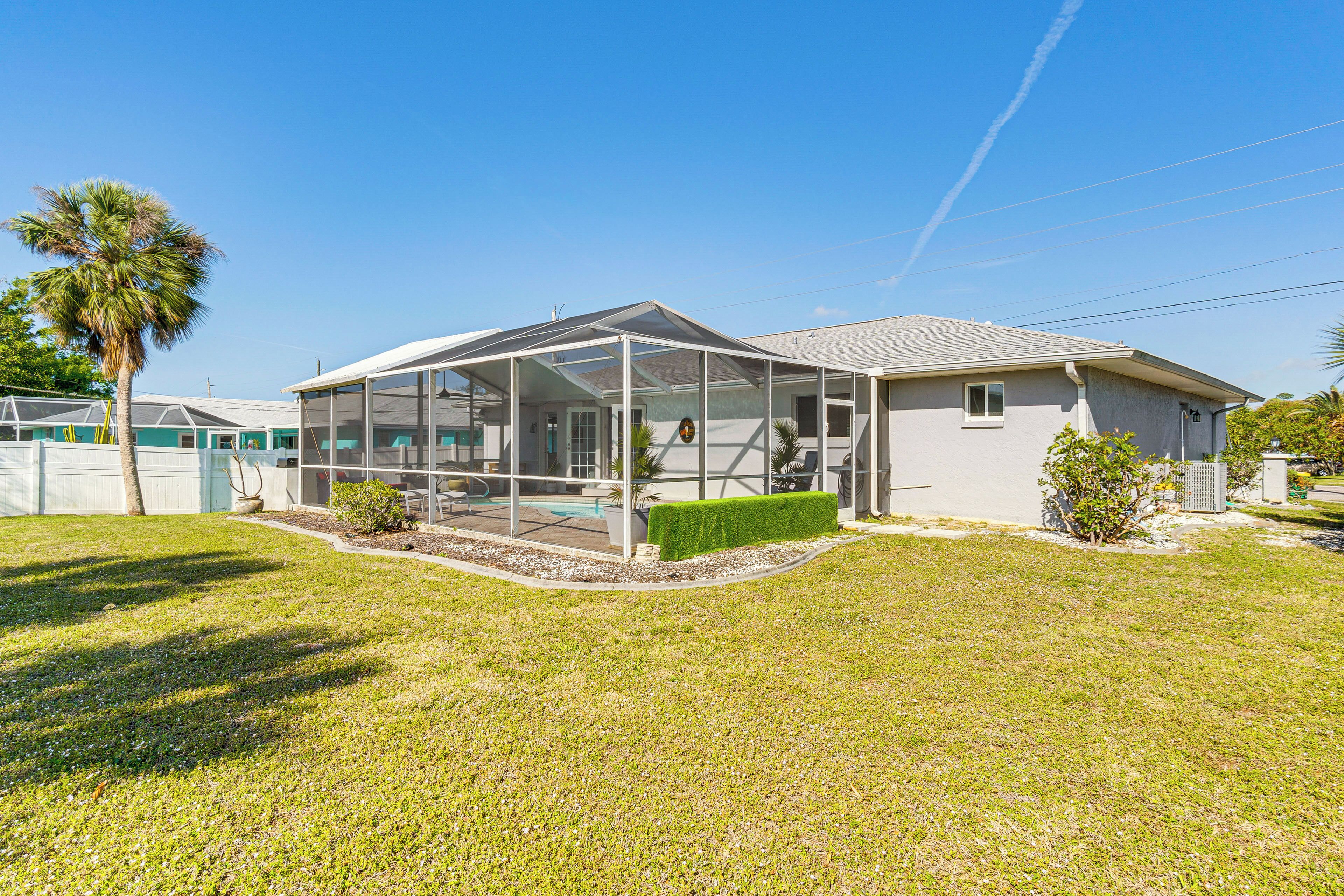 A single-story house with a covered patio, a lawn, and a palm tree.