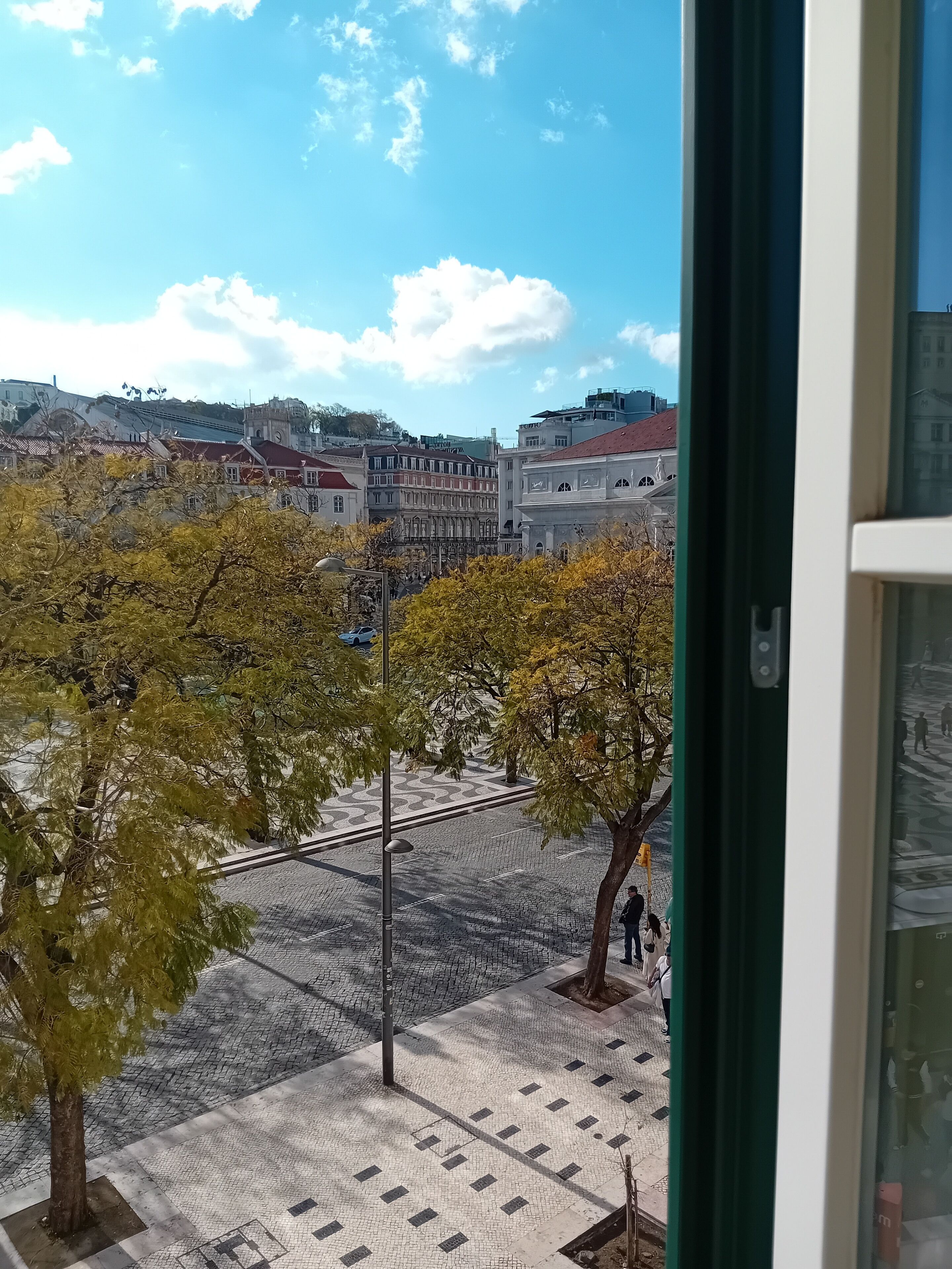 A view from a window overlooking a cityscape with buildings, trees, and a clear sky.
