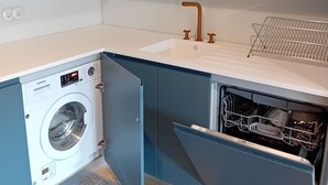 A compact kitchen with a built-in washing machine, a dishwasher, and a sink with a copper faucet.
