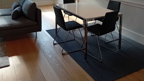 A modern living room with a glass-top dining table, black chairs, a grey sofa, and a large window.