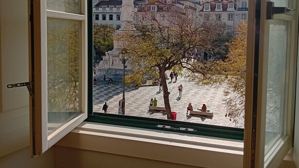 A window with a view of a cityscape, including buildings and a statue.