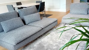 A modern living room with a grey sofa, a dining table, and a kitchen area in the background.