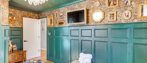 A room with a bed, a bench, a television, and a wall decorated with framed pictures and a floral pattern.