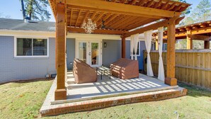 Eine überdachte Terrasse mit einer Pergola, eine überdachte Sitzgelegenheit und ein Blick auf ein Haus im Hintergrund.