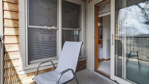 Une véranda couverte avec une chaise en métal, de grandes fenêtres équipées de stores et une porte-fenêtre coulissante donnant sur un espace intérieur.