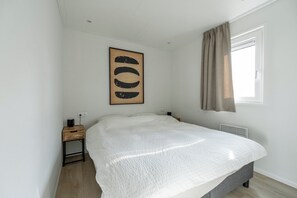 A bedroom with a bed, a nightstand, a wall-mounted artwork, a window with curtains, and a radiator. - Luxury chalet with hot tub in wooded area of the Sallandse Heuvelrug (Haarle)