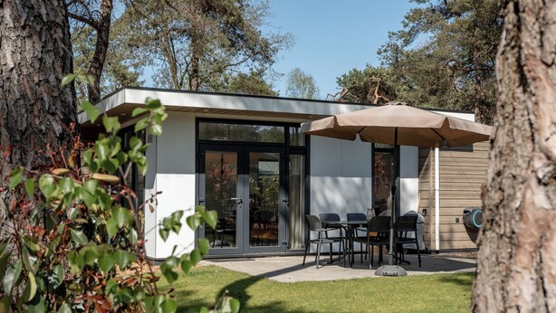Una casa moderna con un patio, mobiliario exterior y una zona cubierta.