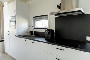 A modern kitchen with a stainless steel sink, a coffee maker, and a window with blinds.