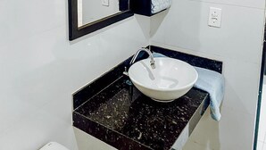 Une salle de bain avec un lavabo blanc, un plan de toilette noir et un miroir à cadre noir.