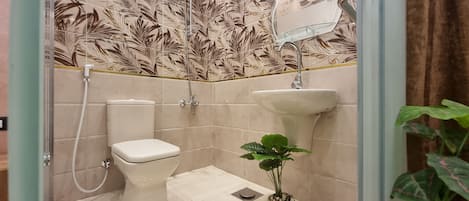 A bathroom with a toilet, shower, sink, and a potted plant.