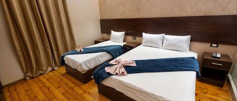 Habitación de hotel con dos camas, suelo de madera, cabecero, mesita de noche y cortina.