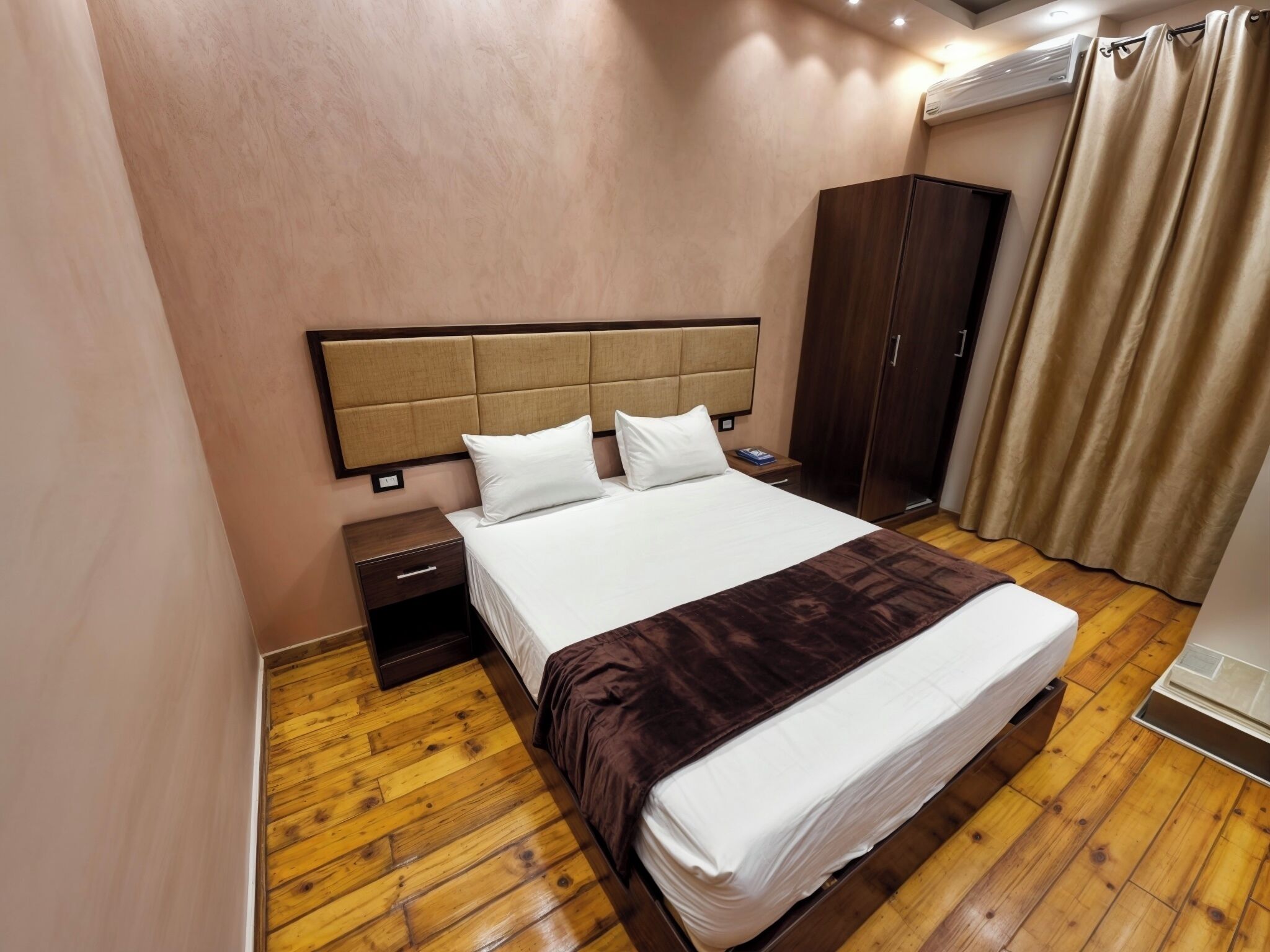Habitación de hotel con una cama grande, suelo de madera, un armario y una mesita de noche.